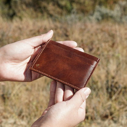 Brown leather wallet held by hands against a blurred natural background