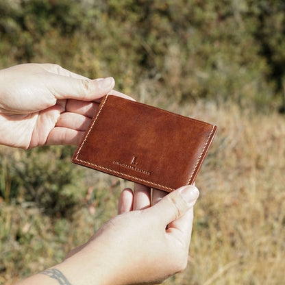 Brown leather wallet held by a person against a natural background